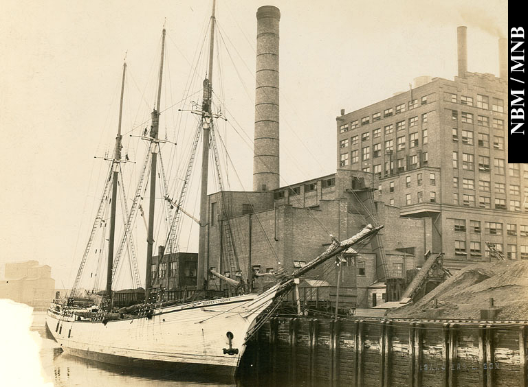 The vessel, "Burpee L. Tucker" at Atlantic Sugar Refineries Limited Wharf showing large coal pile, Saint John, New Brunswick